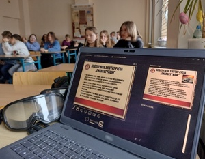 laptop na którym wyświetla się prezentacja, w tle młodzież