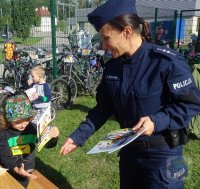 policjanta rozdaje dzieciom książeczki &quot;Bezpieczny Przedszkolak&quot;