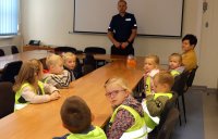 Dzieci w sali słuchają policjanta, który mówi na temat bezpieczeństwa w ruchu drogowym.