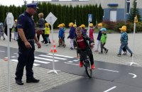Policjant nadzoruje dziecko jadące na rowerze po miasteczku ruchu drogowego.
