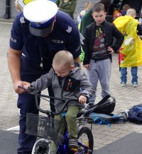 Policjant ruchu drogowego asekuruje chłopczyka jadącego na rowerze po miasteczku ruchu drogowego.