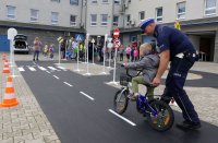 Policjant ruchu drogowego asekuruje chłopczyka jadącego na rowerze po miasteczku ruchu drogowego.