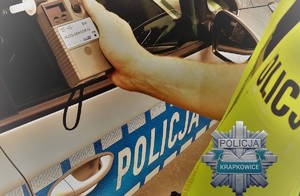 bok radiowozu, ręka policjanta trzymająca w dłoni urządzenie alkosensor do pomiaru stanu trzeźwości