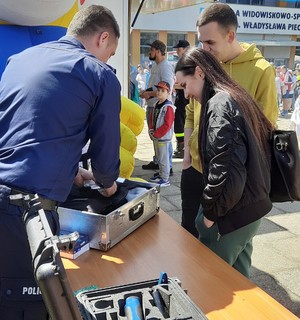 policjant przedstawia kobiecie i mężczyźnie walizkę technika kryminalistyki