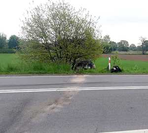 widok miejsca zdarzenia drogowego, jezdnia, krzew, zniszczony granatowy volkswagen w przydrożnym rowie