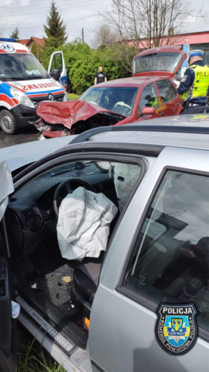 zdjęcie ze zdarzenia drogowego, na którym widać dwa rozbite samochody, karetkę oraz policjanta