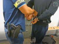 Policjant zakłada zatrzymanemu kajdanki na ręce trzymane z tyłu