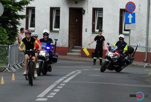 Kolarz na rowerze na trasie wyścigu za nim dwóch policjantów na motocyklach