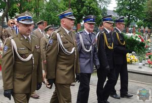Komendant Powiatowy Policji w Oleśnie w asyście przedstawicieli innych służb mundurowych wchodzi na cmentarz komunalny.