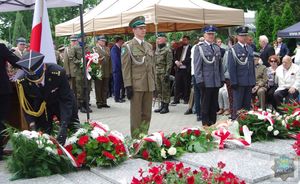 Przedstawiciele służb mundurowych składają wiązankę biało-czerwonych kwiatów na płycie pomnika Powstańców Śląskich