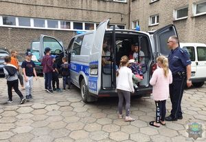 dzieci w towarzystwie policjanta wchodzą do radiowozu w tle inne samochody stojące na parkingu