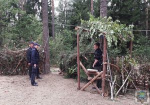 funkcjonariusze opuszczają pole namiotowe, żegna ich harcerz stojący na posterunku przy bramie. Elementy zbudowane z gałęzi drzew iglastych, zadaszenie posterunku z liści.
