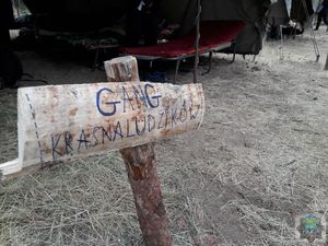 drewniana deska na paliku z napisem &quot; gang krasnoludzików&quot; tuż za nią fragment otwartego szarego namiotu