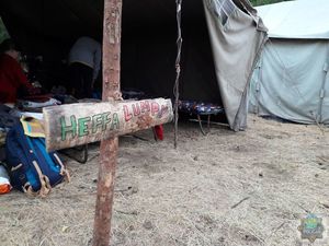 drewniana deska na paliku z napisem &quot; hefa lumpy&quot; tuż za nią otwarty  szary namiot, wewnątrz  dwie osoby.