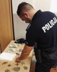 Mężczyzna ubrany w policyjny mundur przelicza pieniądze rozłożone na stole.