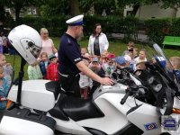 Stojący przy motocyklu policyjnym funkcjonariusz ruchu drogowego, prezentujący dzieciom motocykl
