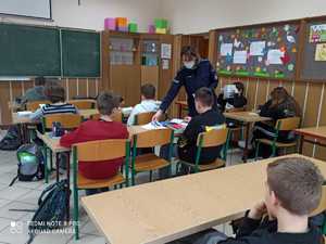 Policjantka rozdaje dzieciom w klasie ulotki i broszury informacyjne dotyczące dzielnicowych.
