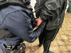 policjantka prowadzi zatrzymanego mężczyznę, ten ma na rękach kajdanki