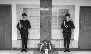 2 policjantów stoi na baczność przed pamiątkową tablicą