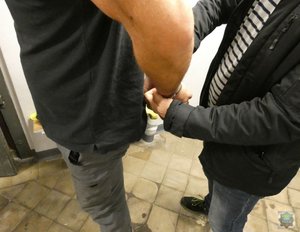 Zatrzymany mężczyzna, z kajdankami na rękach prowadzony przez policjanta.