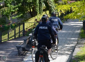 policjanci jada jeden za drugim na rowerach wzdłuż  ścieżki rowerowej w parku