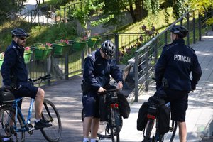 policjanci z drużyny rowerowej stoją obok siebie, jeden z nich poprawia swoją sakwę na rowerze