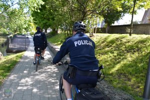 na pierwszym planie policjant na rowerze (zdjęcie od tyłu) w głębi drugi policjant na rowerze