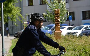 profil policjanta na rowerze, w tle budynek i drewniana rzeźba