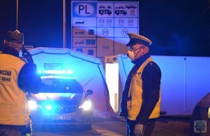 policjant stoi na tle radiowozu i znaku drogowego