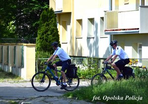 2 policjantów na rowerach jedzie ulicą obok blok mieszkalny