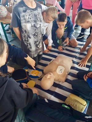 Na zdjęciach znajdują się dzieci i policjantka. osoby ćwiczą między innymi na manekinie udzielania pierwszej pomocy.