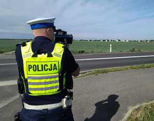 Zdjęcie przedstawia policjanta stojącego z radarem przy drodze.