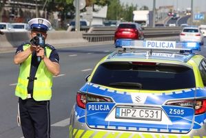 Policjant stoi z radarem obok radiowozu.