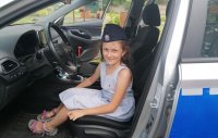 W radiowozie siedzi dziewczynka w czapce policyjnej