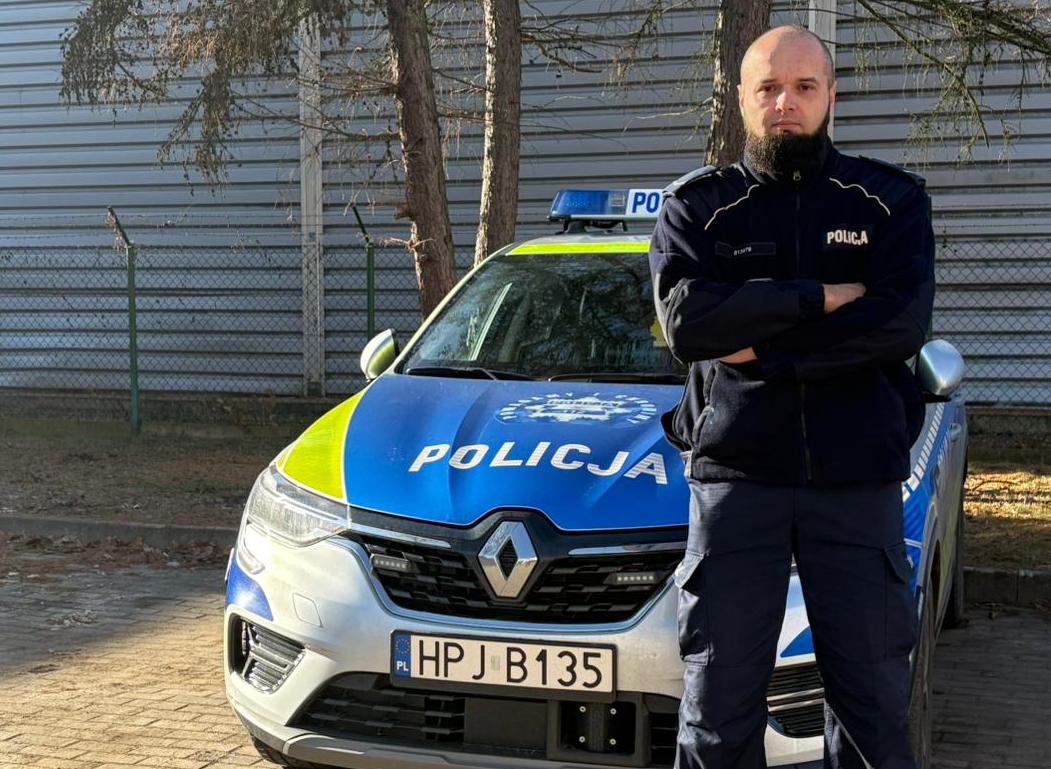 policjant w mudurze stoi przed radiowozem