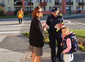 w rejonie przejścia dla pieszych umundurowana policjantka przekazuje odblaski dzieciom