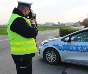 policjant podczas pracy na ręcznym mierniku prędkości, w tle oznakowany radiowóz