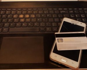 Na klawiaturze laptopa leży telefon komórkowy i karta płatnicza