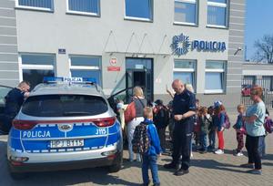 dzieci stoją przed komisariatem policji i oglądają radiowóz