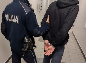 policjanci prowadzą zatrzymanego mężczyznę w kajdankach zapiętych na ręce trzymane z tyłu
