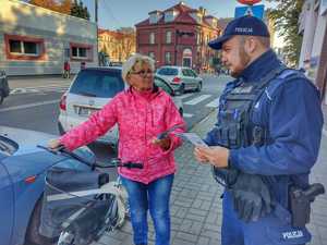 umundurowany policjant rozdaje elementy odblaskowe i ulotki edukacyjne