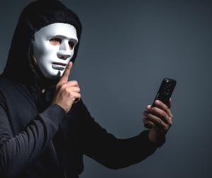 mężczyzna w białej masce, czarnej bluzie, w ręku trzyma telefon