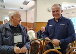 policjant przekazuje ulotkę seniorowi
