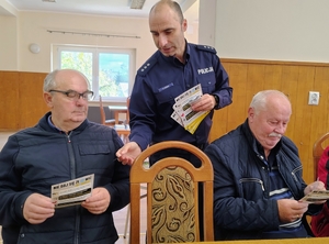 policjant przekazuje materiały edukacyjne senirowi