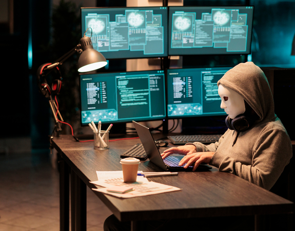 osoba w białej masce w pomieszczeniu z monitorami