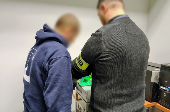 policjant pobiera odciski palców zatrzymanemu mężczyźnie