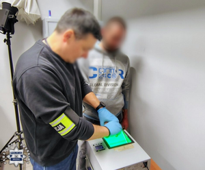 policjant pobiera odciski palców zatrzymanemu