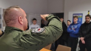 policjant w mundurze instruktora strzelectwa  pokazuje broń młodzieży