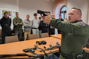 policjant w mundurze instruktora strzelectwa  pokazuje broń młodzieży