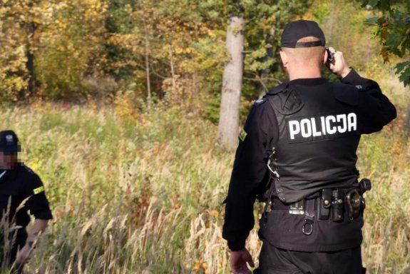 Umundurowany policjant prowadzi poszukiwania w terenie leśnym